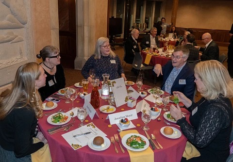 Faculty members sitting around a table socializing and eating at the Faculty Decades Dinner Event.